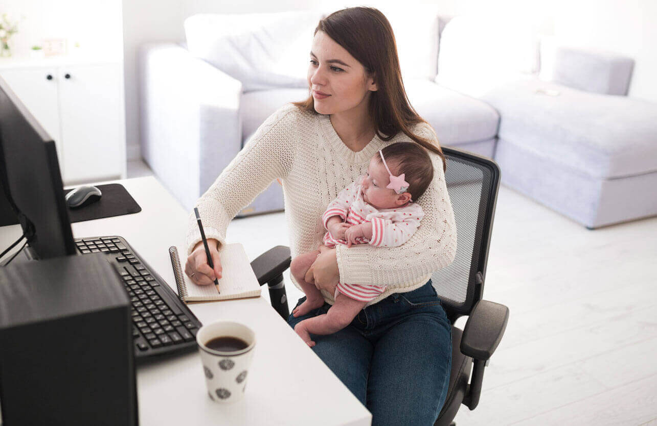 Femme au bureau travaillant sur un ordinateur avec son bébé dans les bras