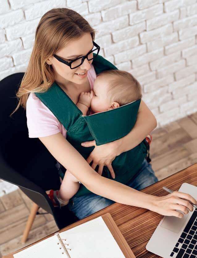 Femme travaillant sur PC avec son enfant dans un porte-bébé