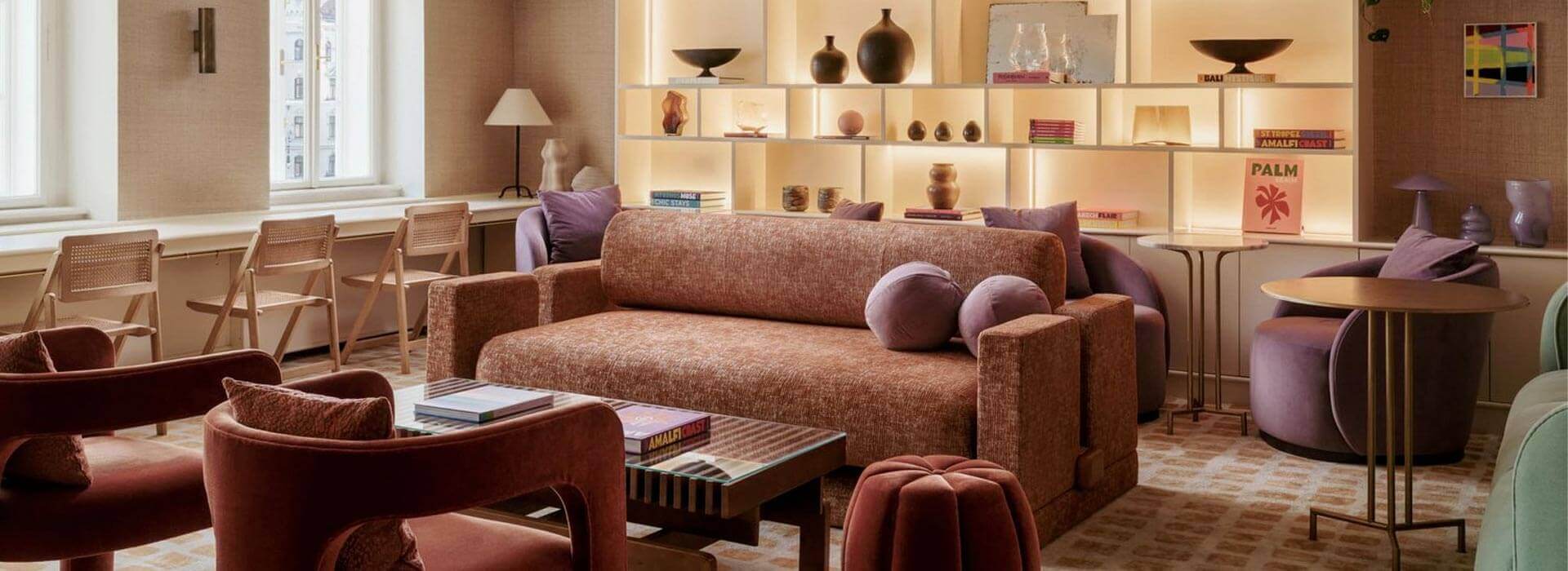 Aménagement hôtel télétravail photo d'un aménagement hôtel am hof 8 à Vienne : vue sur canapé confortable aux couleurs chaudes (tons roses / orangés) avec table basse en bois et verre ainsi qu'une grande bibliothèque intégrée en arrière-plan